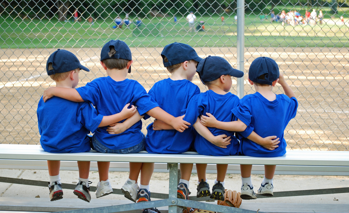 five little boys put their arms around each other befor their baseball game